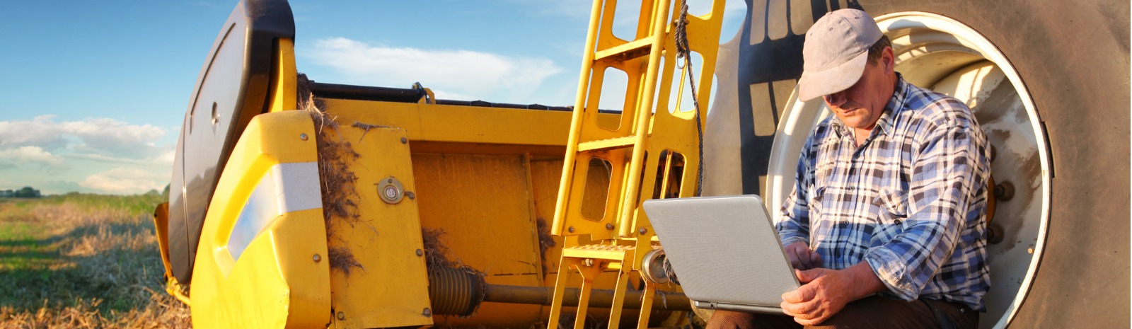 Man sitting on tractor tire while on a laptop