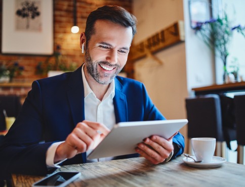 Man in cafe drinking coffee working on a tablet.