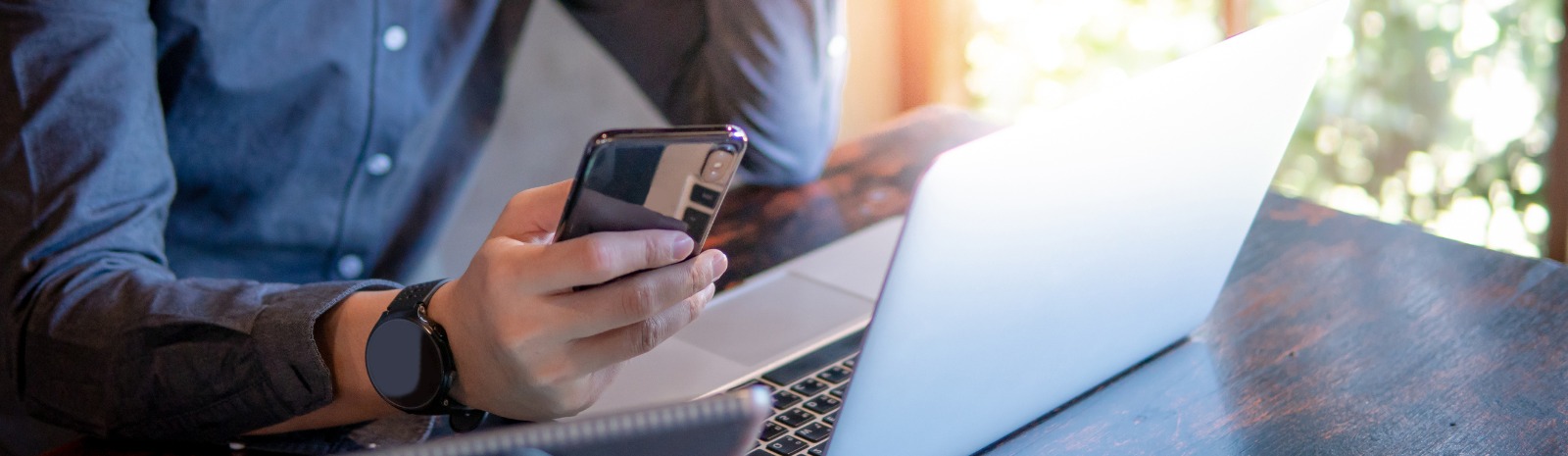 Man's hand using a cell phone with a laptop open